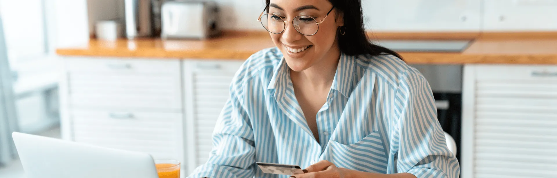 A woman in a kitchen smiling at a computer screen.